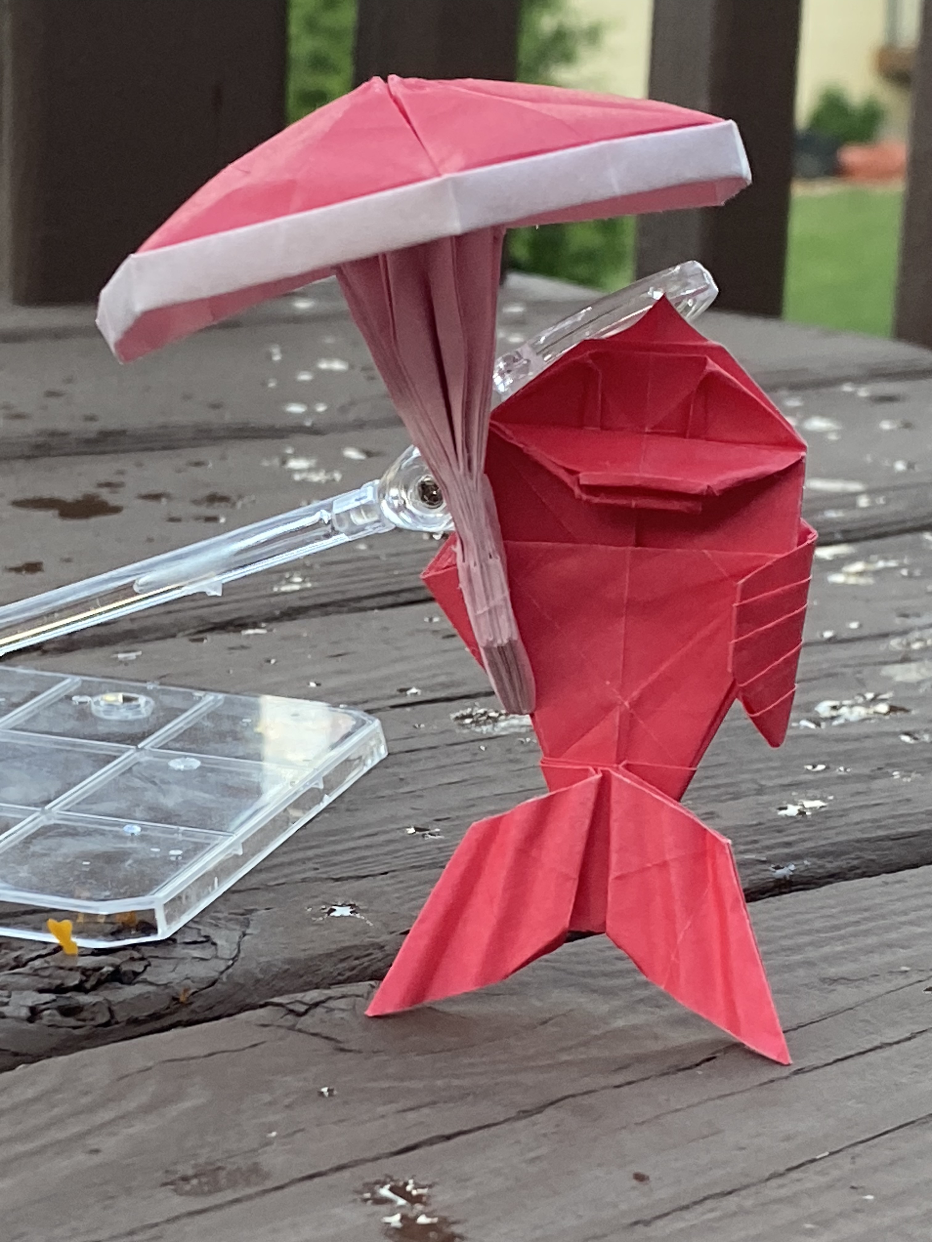 Origami fish holding an umbrella.